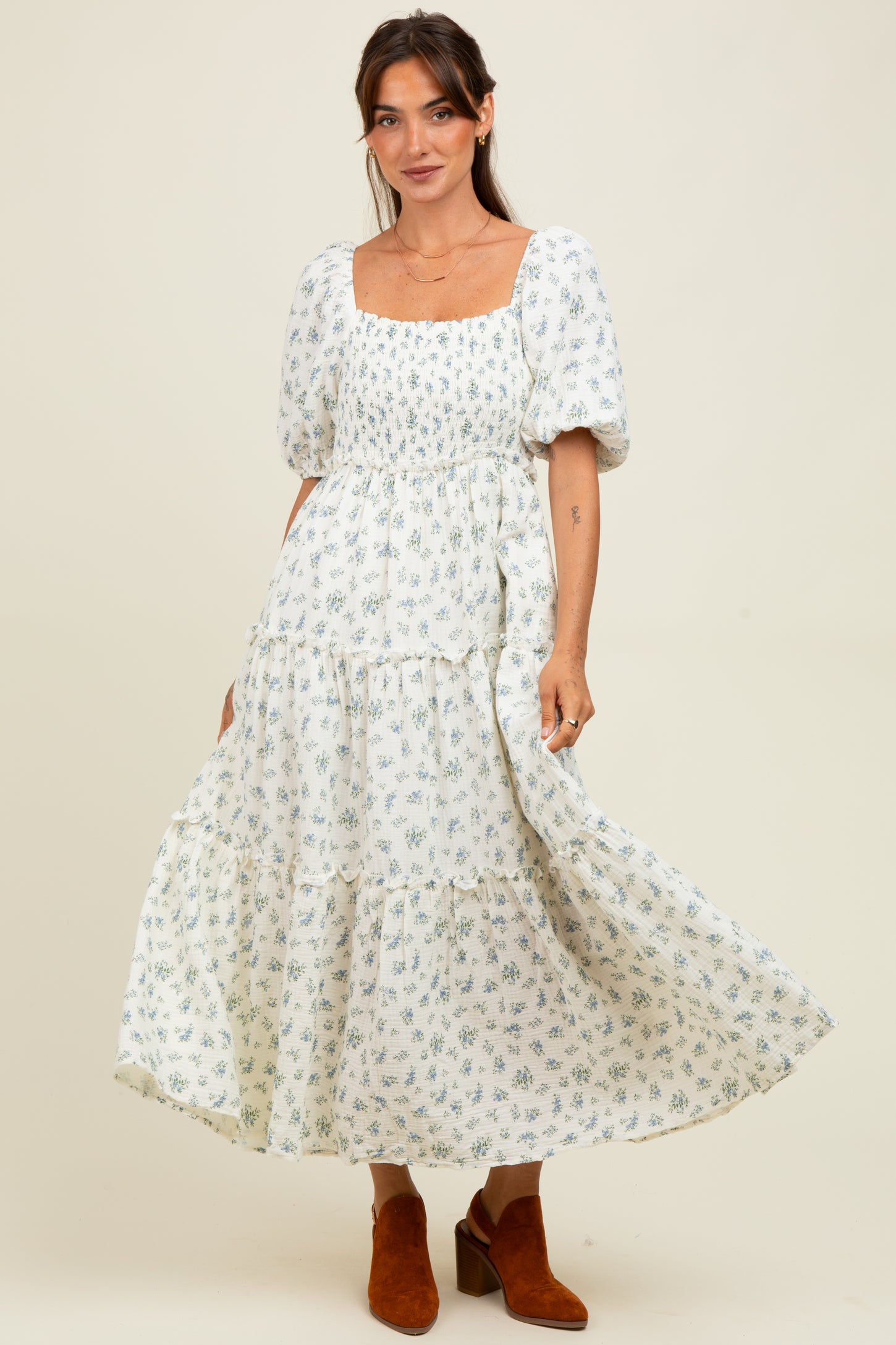 woman wearing a white floral maxi dress with puff sleeves and a square neckline, paired with brown ankle boots