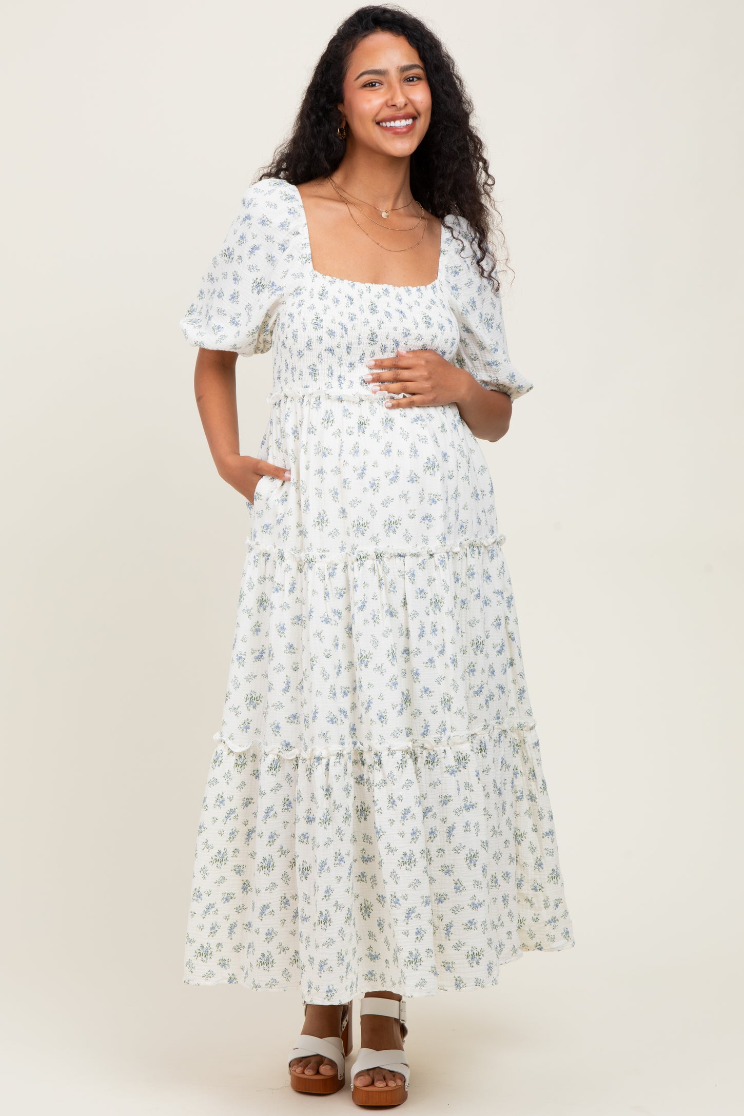 woman wearing a white floral maternity maxi dress with a square neckline and short puff sleeves, holding her baby bump