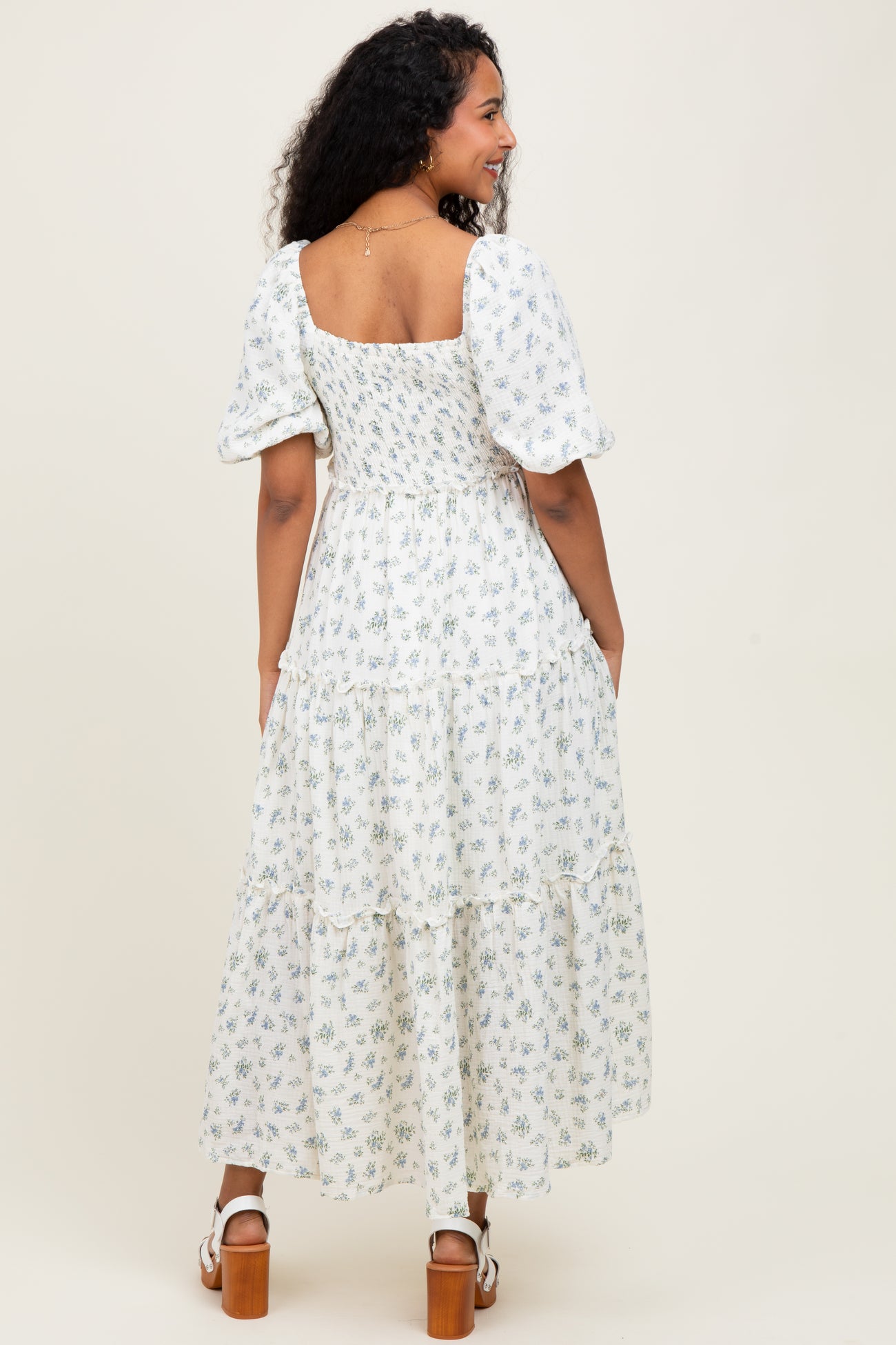 woman wearing a white floral print maternity maxi dress with puff sleeves and a tiered skirt