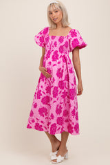 woman wearing a bright pink floral maternity dress with puff sleeves and a baby bump