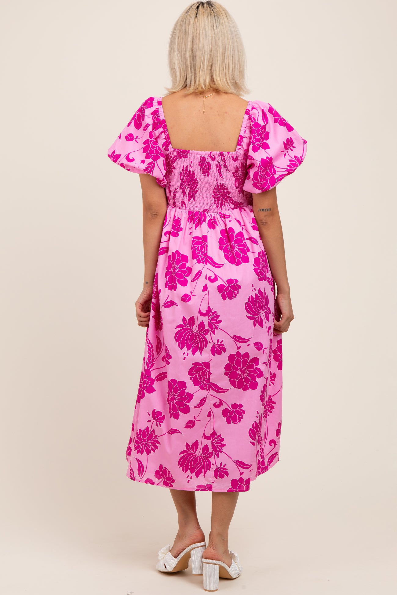 woman wearing a pink floral print maternity dress with short puff sleeves and a smocked bodice, showing a baby bump from the back