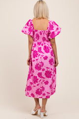 woman wearing a pink floral print maternity dress with short puff sleeves and a smocked bodice, showing a baby bump from the back