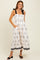 woman wearing a white floral print midi dress with black straps and pockets, standing against a neutral background