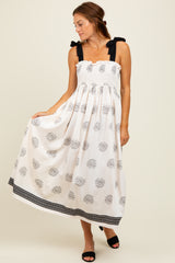 woman wearing a white floral maxi dress with black tie straps and a gathered bodice