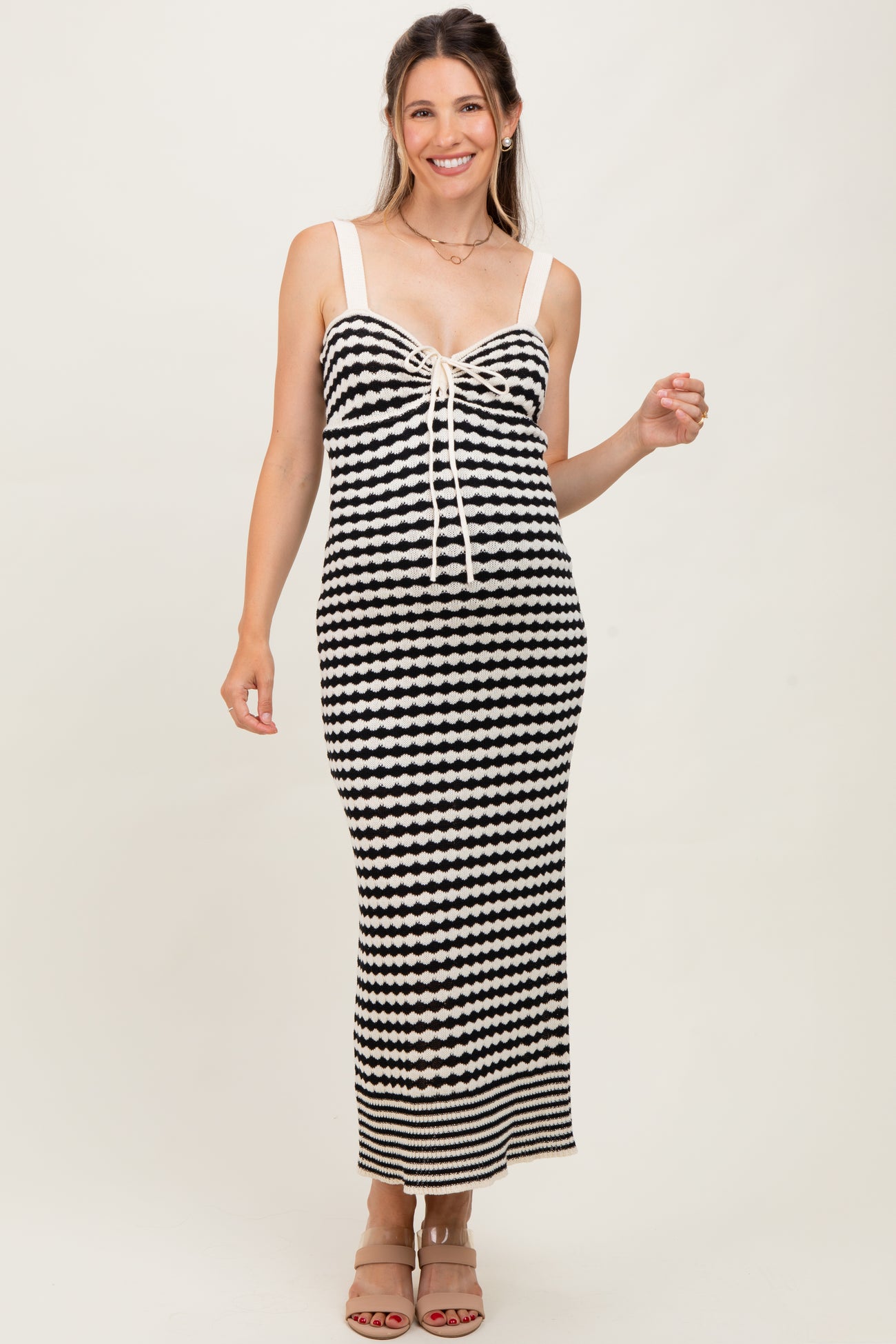 woman wearing a black and white striped maternity maxi dress with a tie front and spaghetti straps, showing off her baby bump