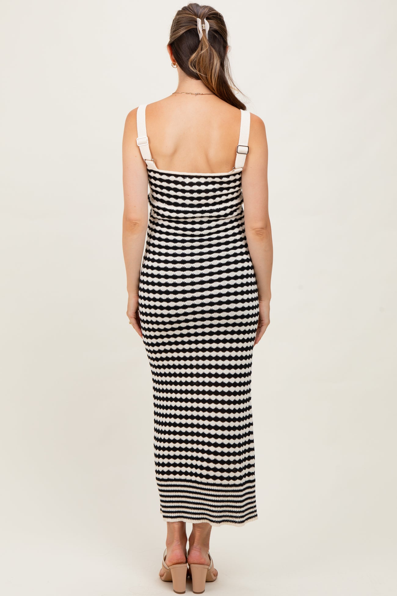 woman wearing a black and white striped maternity maxi dress with spaghetti straps, showing a fitted silhouette from the back