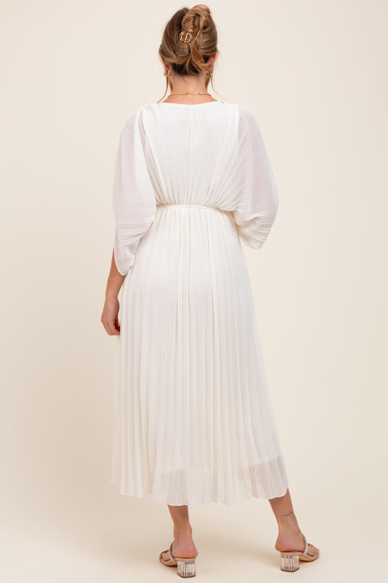woman wearing a white pleated maternity dress with a relaxed fit, showcasing a flowing silhouette and half sleeves