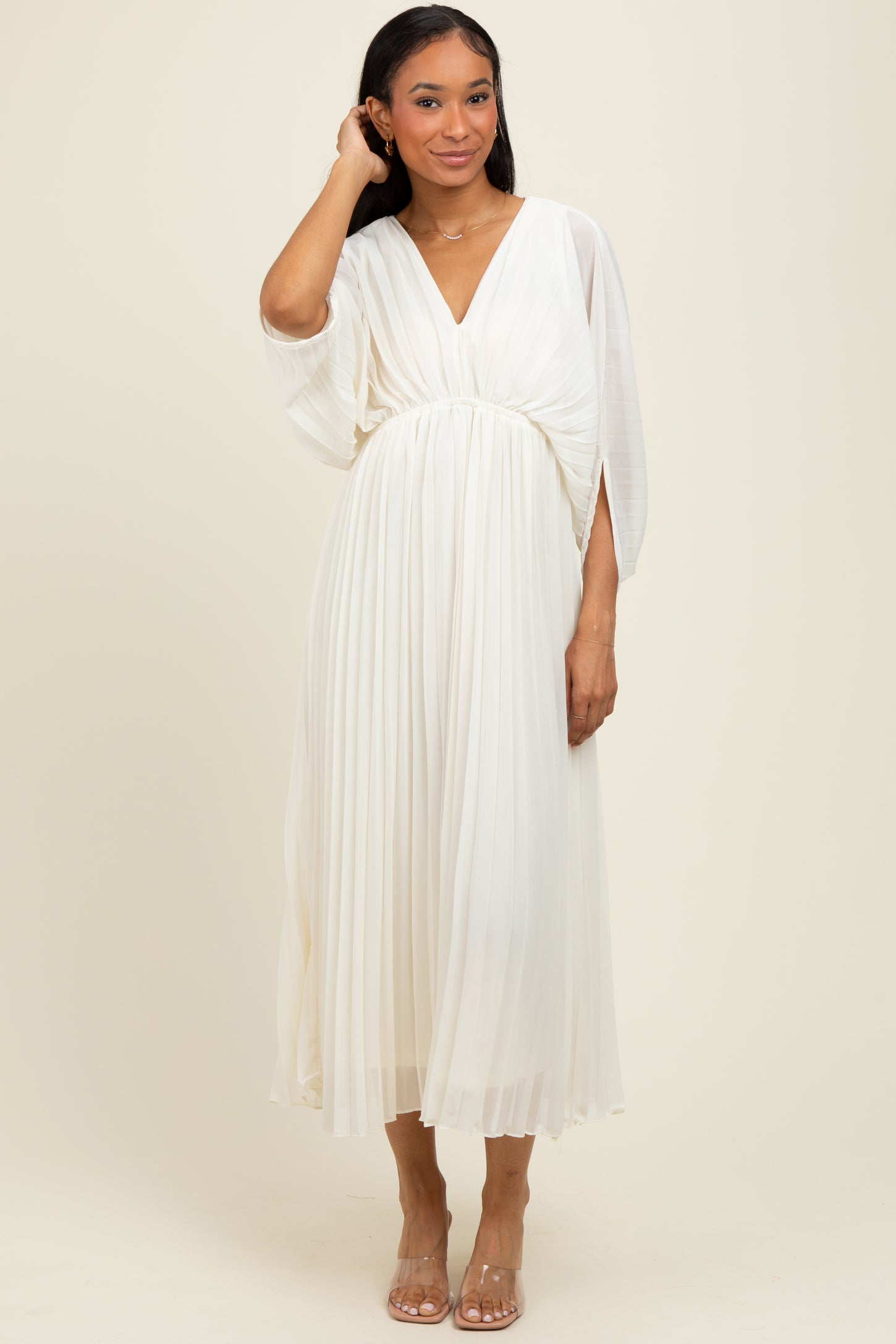 woman wearing a flowing white pleated midi dress with a deep v-neck and batwing sleeves