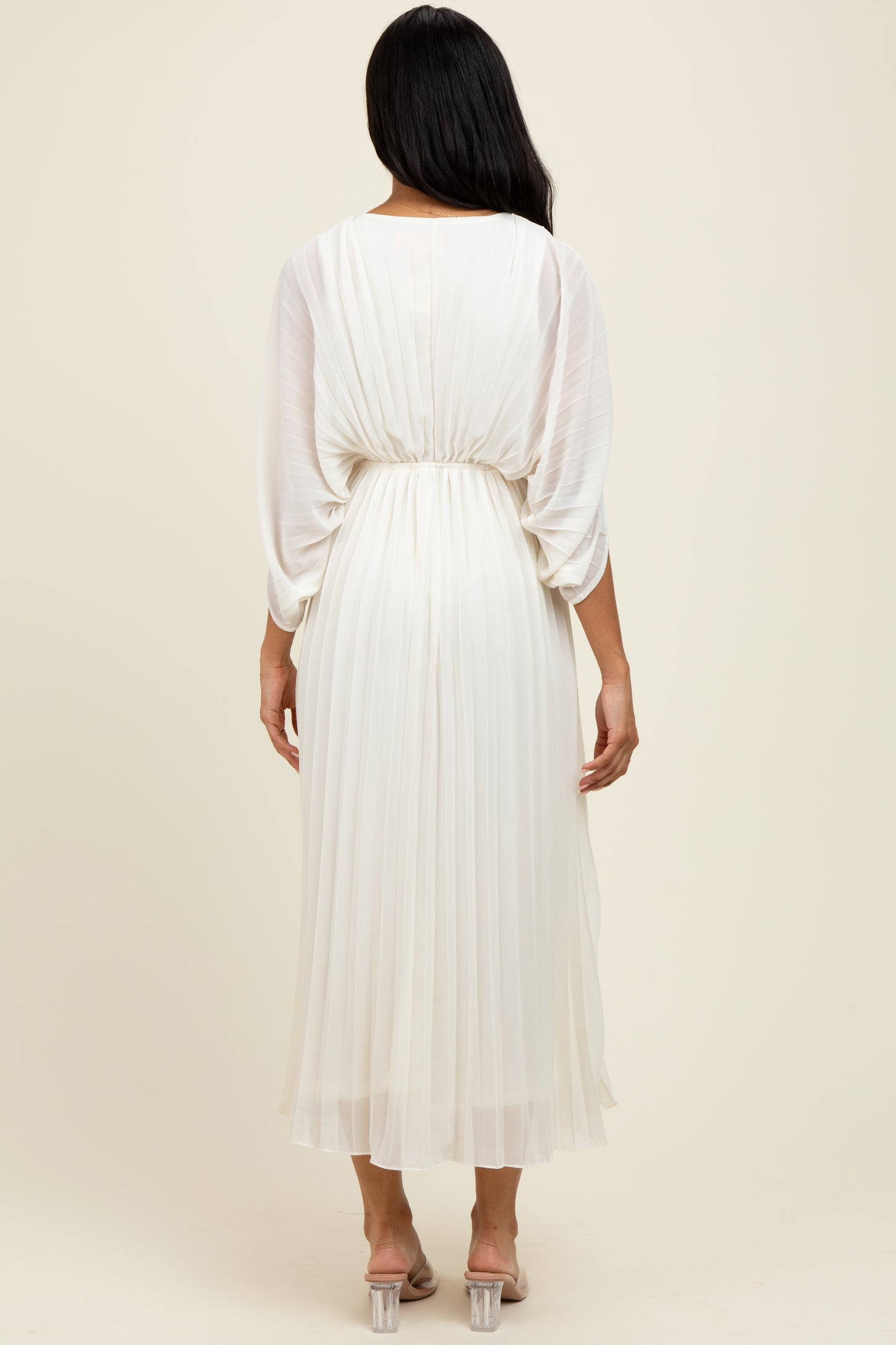 woman wearing an elegant white pleated midi dress with a cinched waist and long sleeves, viewed from the back