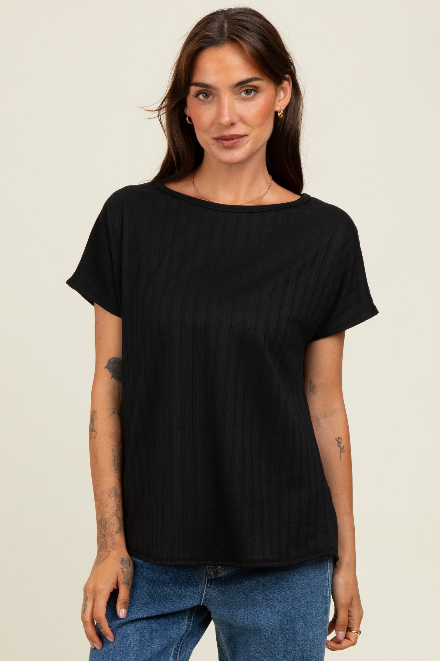 woman wearing a black short sleeve ribbed top with a relaxed fit, standing in front of a neutral background