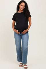 woman wearing a black ribbed maternity top and blue jeans, gently cradling her baby bump