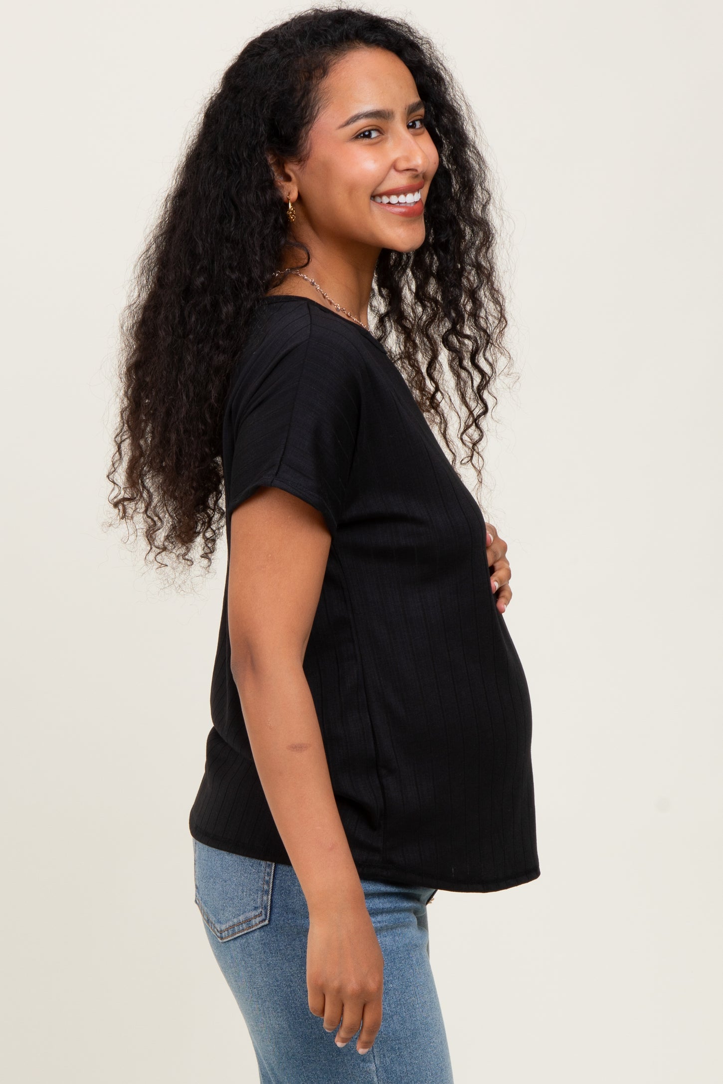 woman wearing a black ribbed maternity top and showing her baby bump, paired with blue jeans