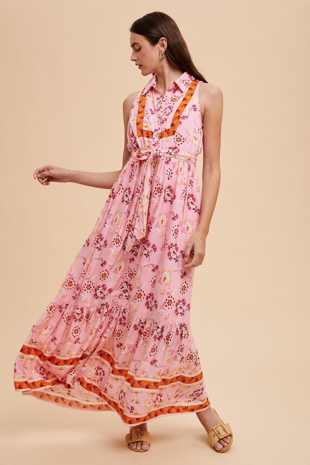 woman wearing a sleeveless pink maxi dress with a floral pattern and bow tie detail at the neckline