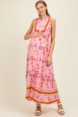 woman wearing a pink floral maxi maternity dress with a belted waist and a flowing silhouette, showcasing her baby bump