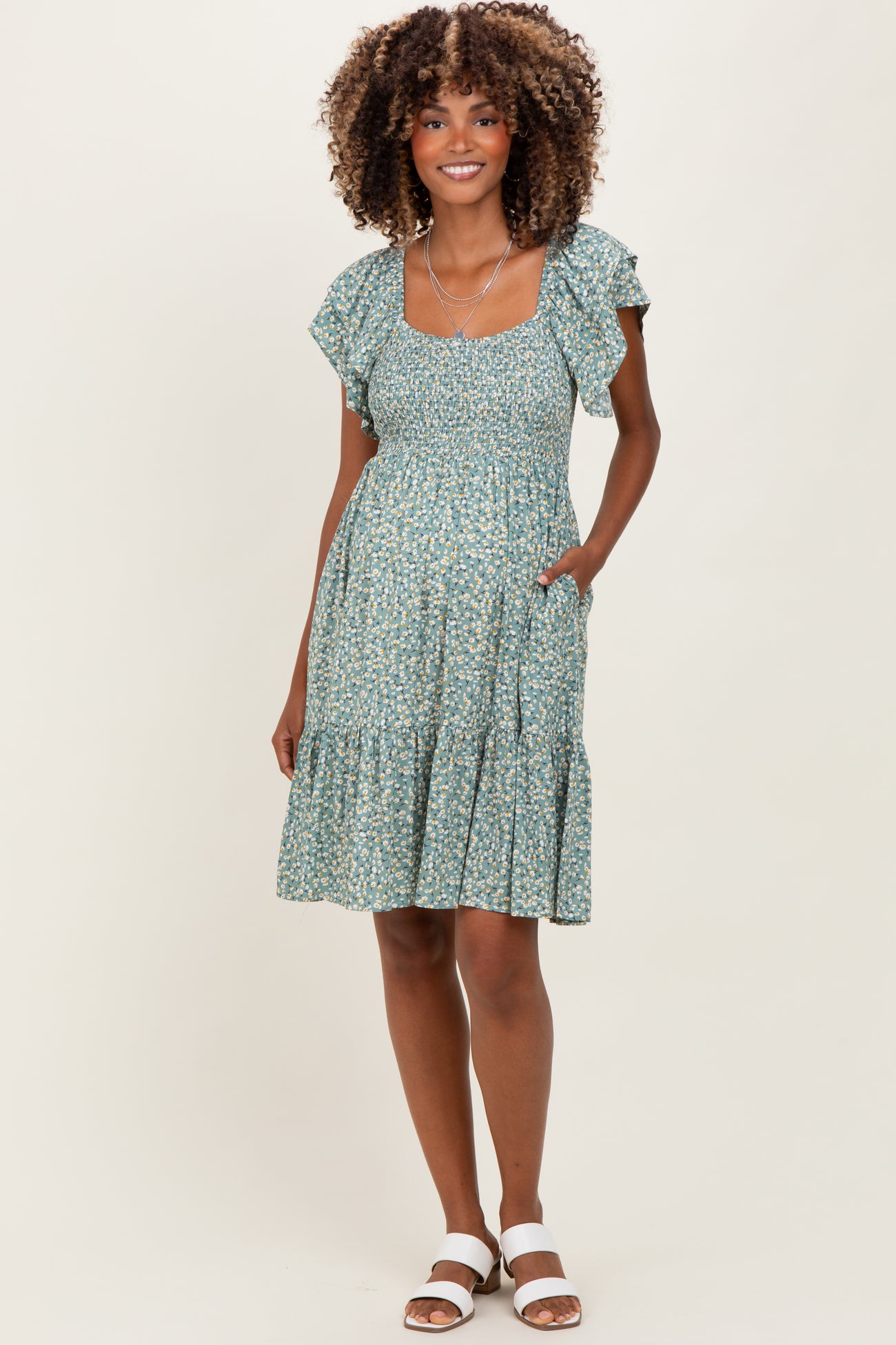 woman wearing a green floral maternity dress with ruffled sleeves and a tiered skirt