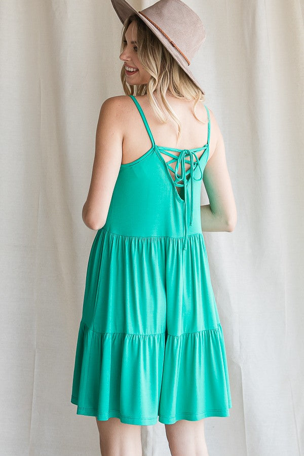woman wearing a teal backless sundress with a tied detail and a flared skirt, paired with a wide-brimmed hat