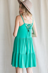 woman wearing a teal backless sundress with a tied detail and a flared skirt, paired with a wide-brimmed hat