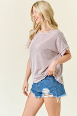 woman wearing a light taupe striped short sleeve top and distressed denim shorts, smiling and posing to the side