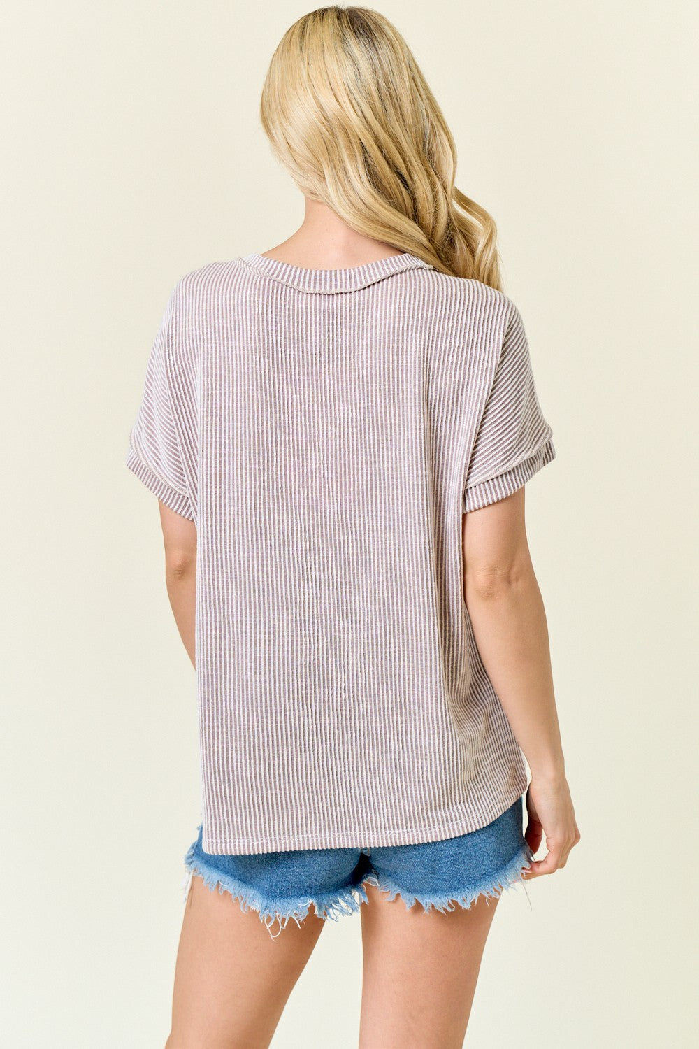 woman wearing a loose-fitting mauve striped t-shirt with rolled sleeves and paired with blue denim shorts
