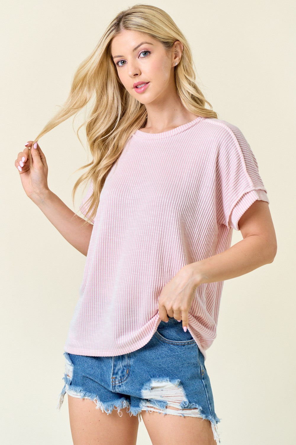 woman wearing a light pink ribbed short sleeve top paired with distressed denim shorts