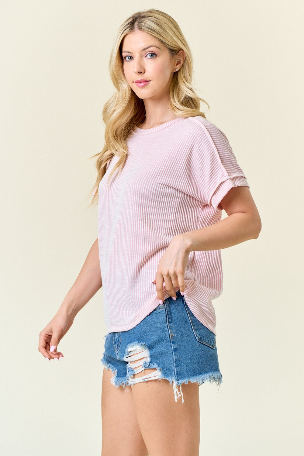 woman wearing a light pink ribbed short sleeve top and distressed denim shorts