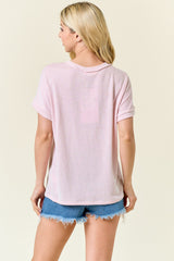 woman wearing a light pink ribbed short sleeve top paired with denim cut-off shorts, viewed from the back