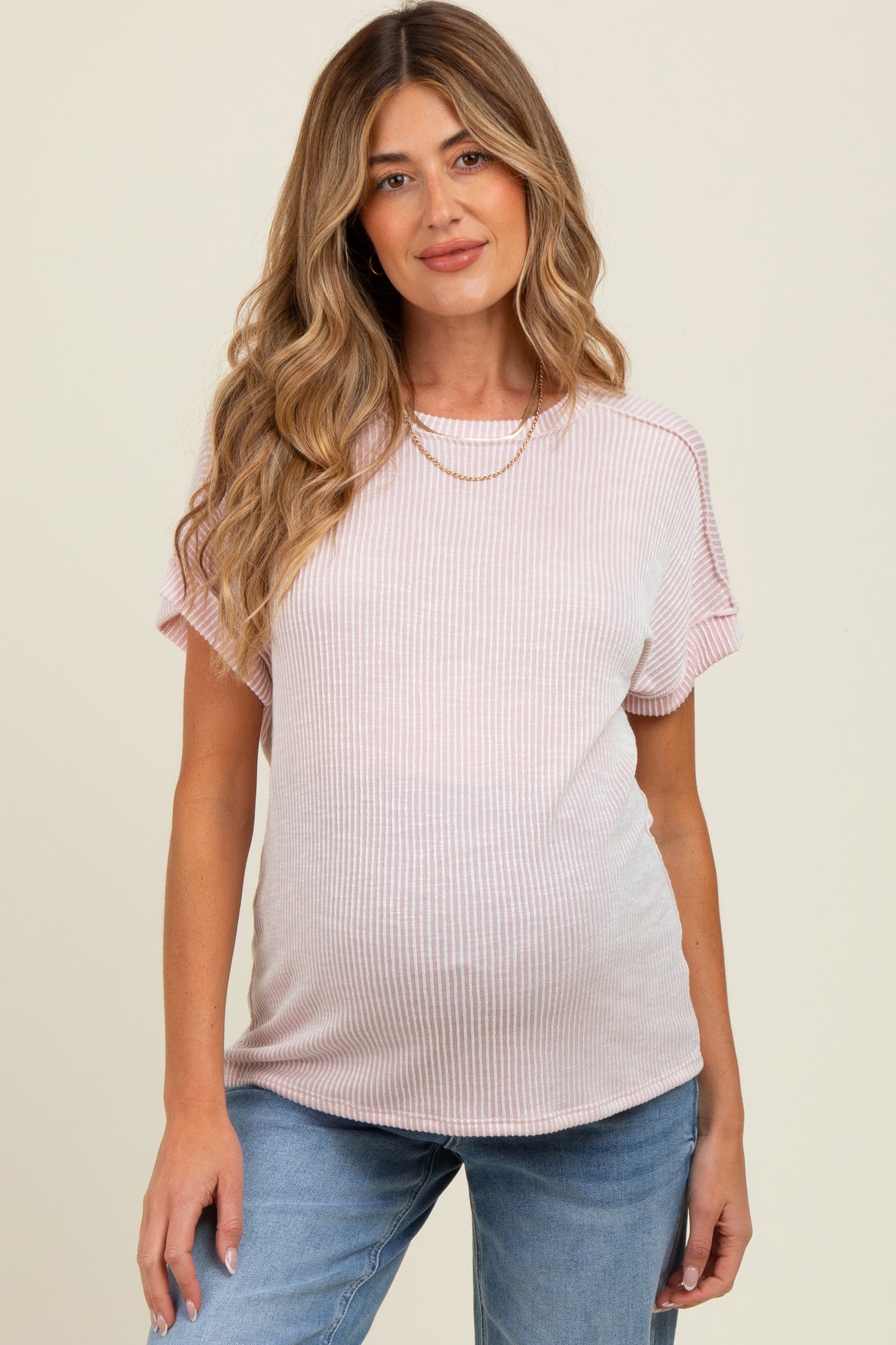 woman wearing a light pink striped maternity top and showing her baby bump with casual jeans