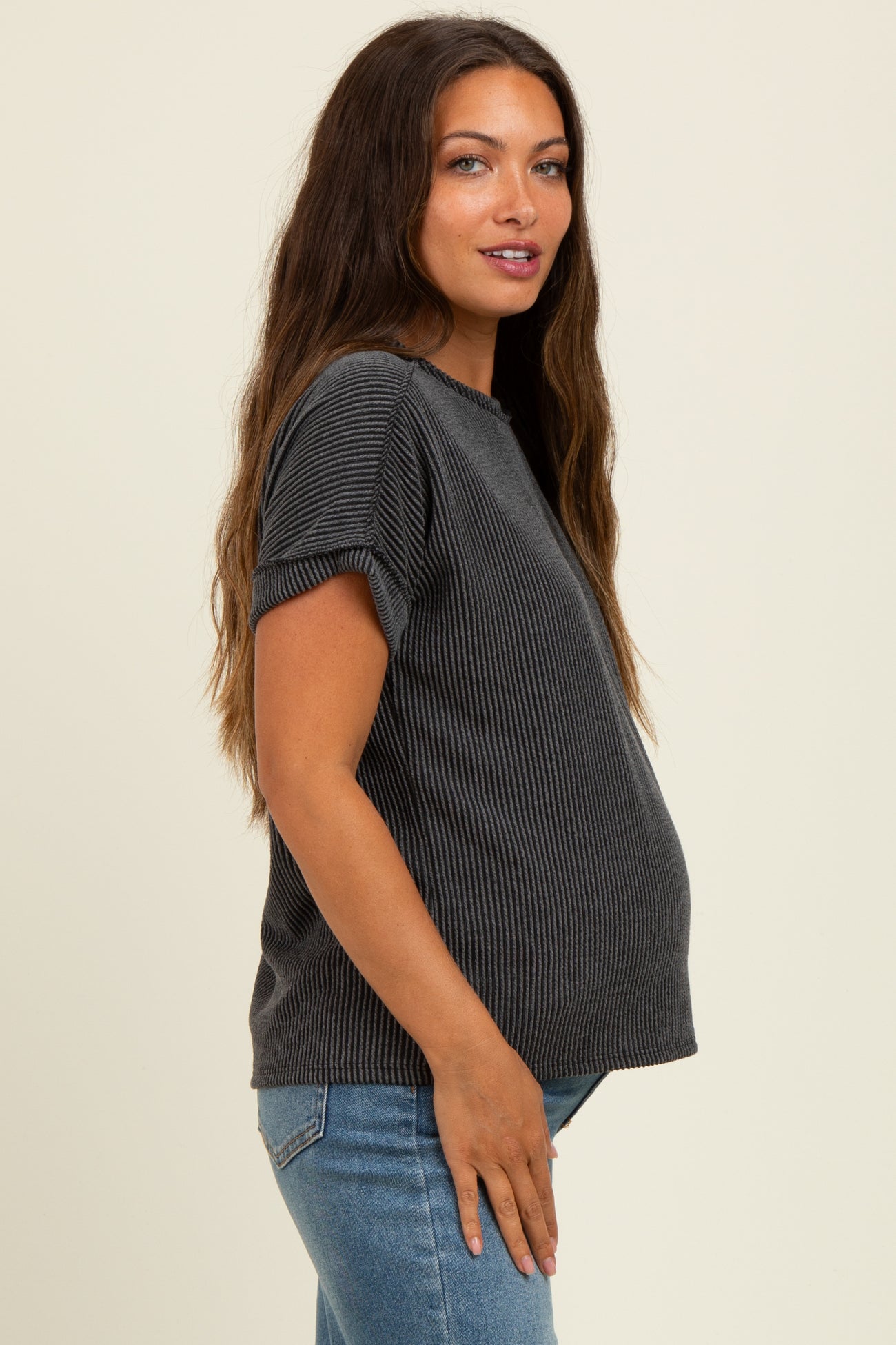 woman wearing a ribbed gray maternity top and showing her baby bump while standing sideways