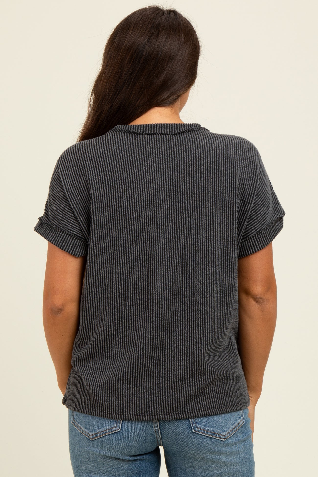 woman wearing a dark gray ribbed maternity top with rolled sleeves, showing the back view and paired with blue jeans