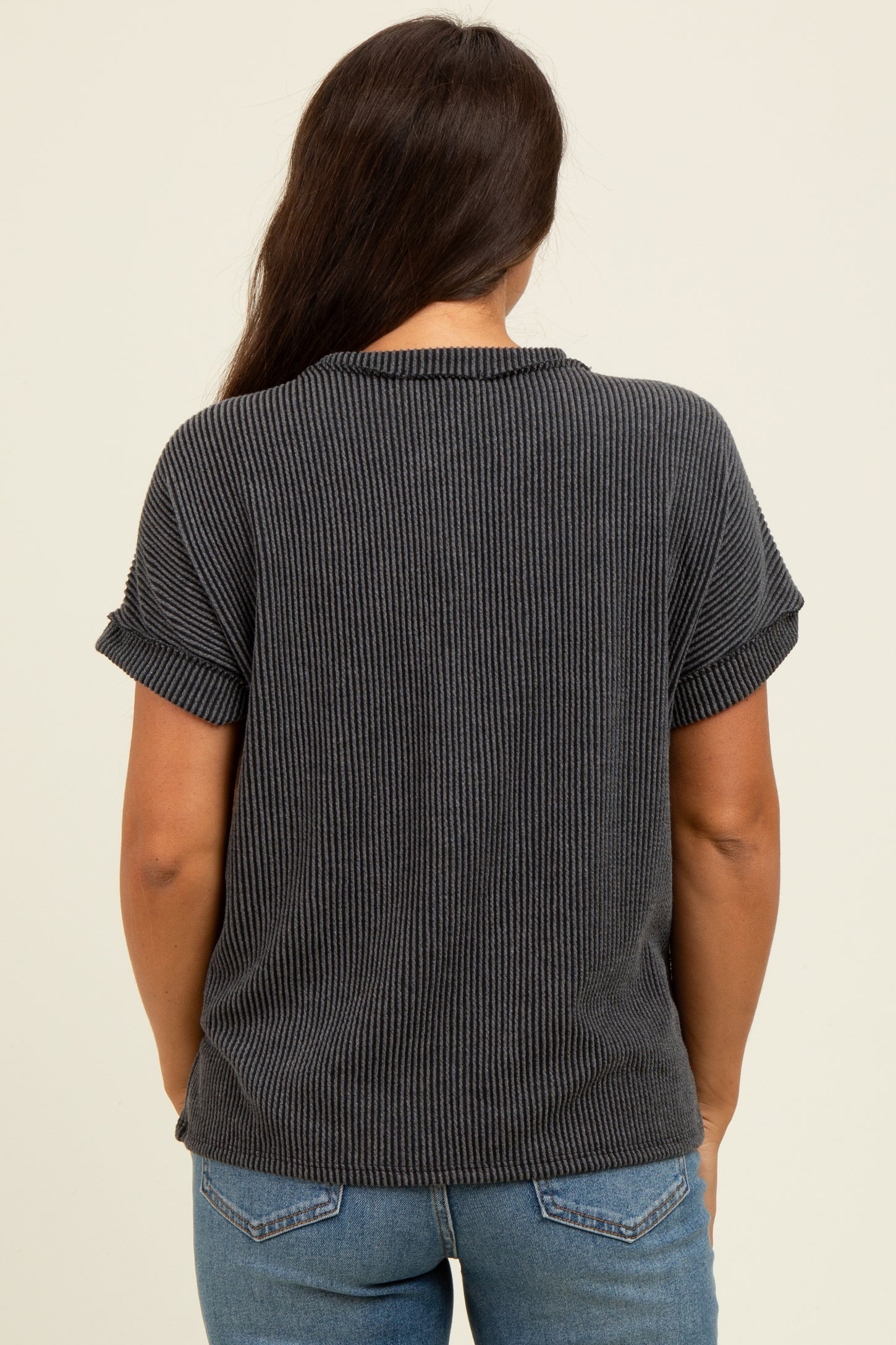 woman wearing a dark gray ribbed maternity top with rolled sleeves, showing the back view and paired with blue jeans