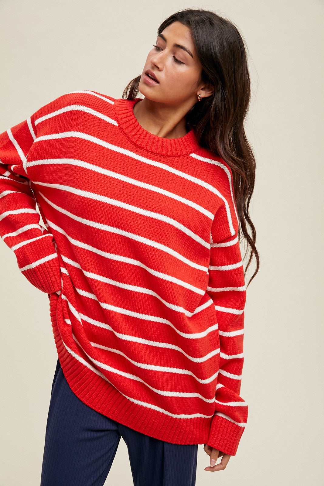 woman wearing a red and white striped oversized sweater with a ribbed neckline and side slit, paired with navy pants