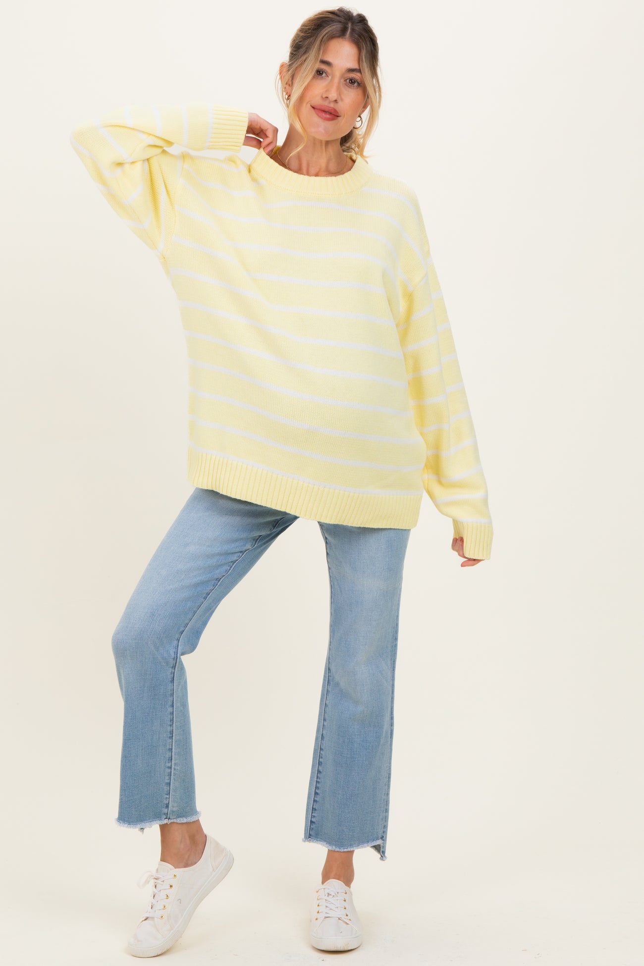 woman wearing a yellow striped oversized maternity sweater and blue flared jeans