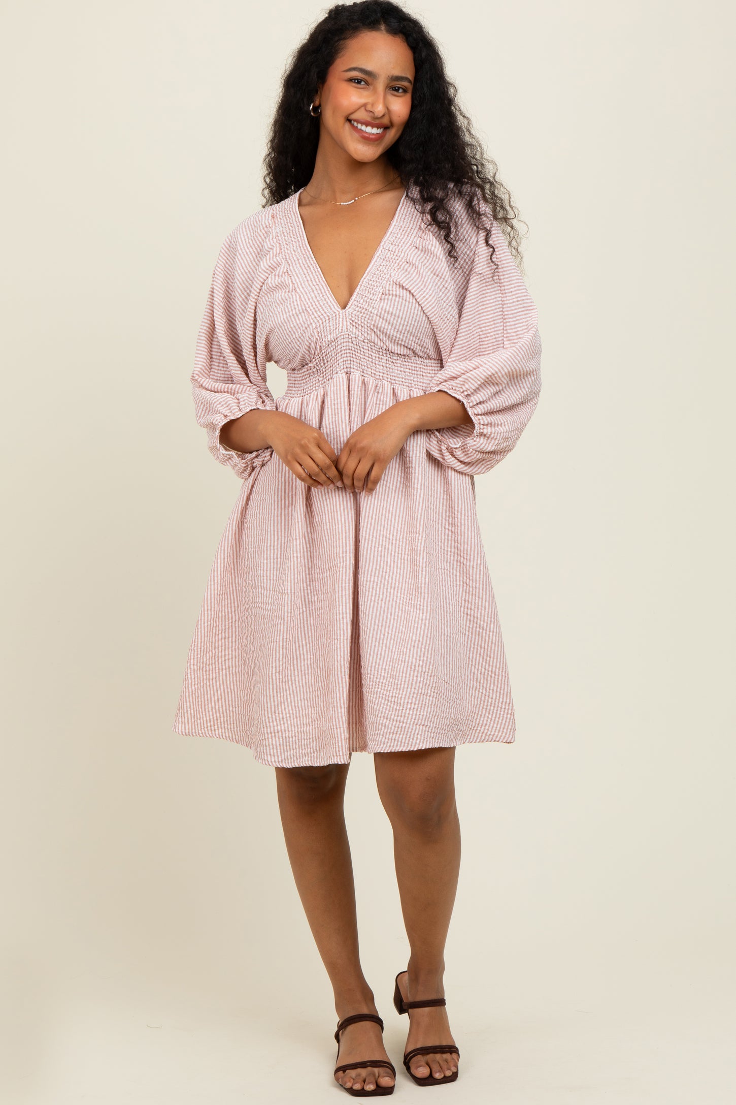 woman wearing a pink and white striped short dress with a deep v-neck and puff sleeves