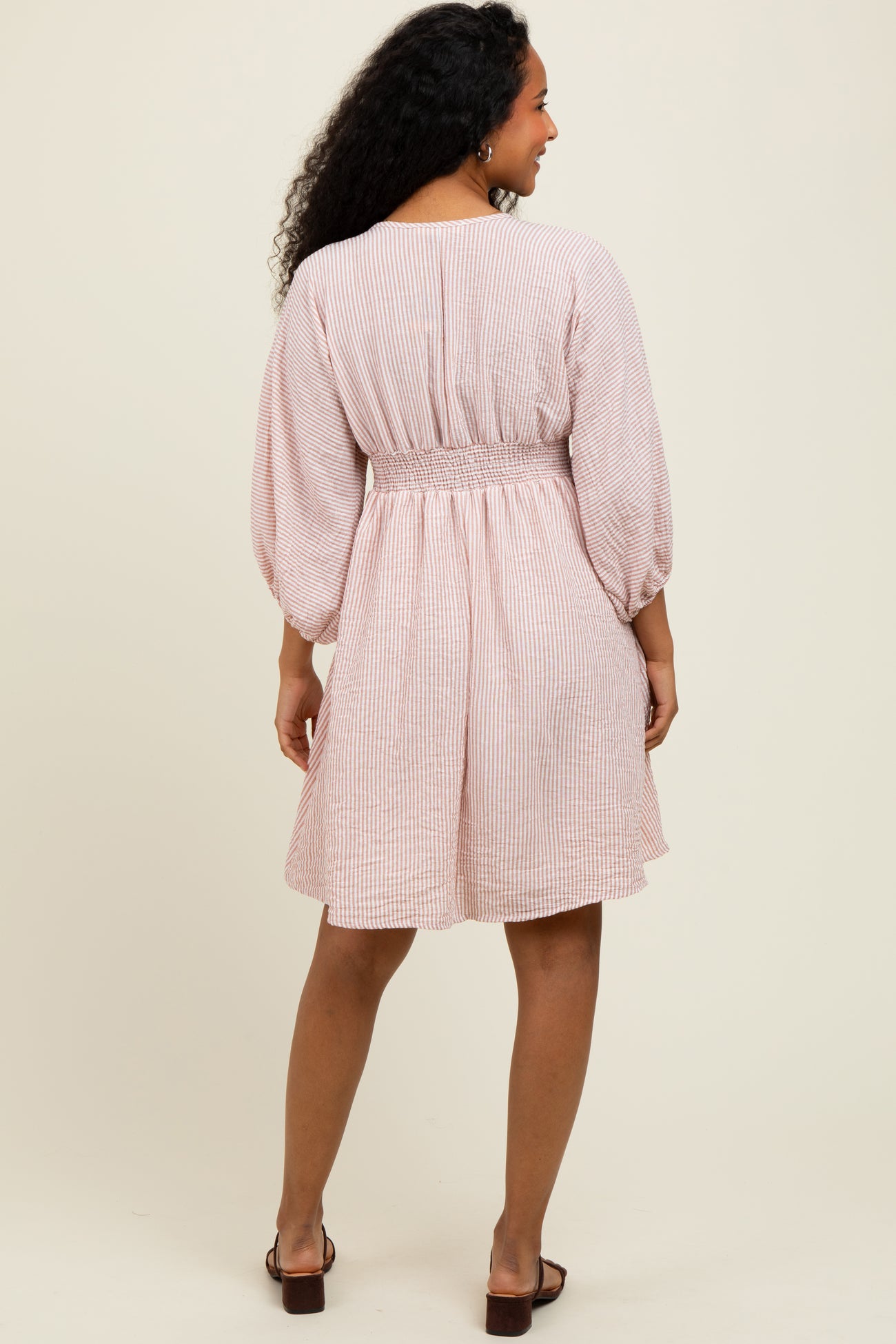 woman wearing a pink and white striped short sleeve dress with a smocked waist and balloon sleeves, shown from the back