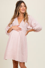 woman wearing a striped pink maternity dress with a deep v-neck and puff sleeves, holding her baby bump