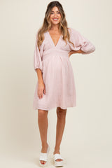 woman wearing a pink and white striped maternity dress with a deep v-neck and balloon sleeves, showing off her baby bump