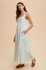 woman wearing a light blue floral maxi dress with pockets and spaghetti straps on a neutral background