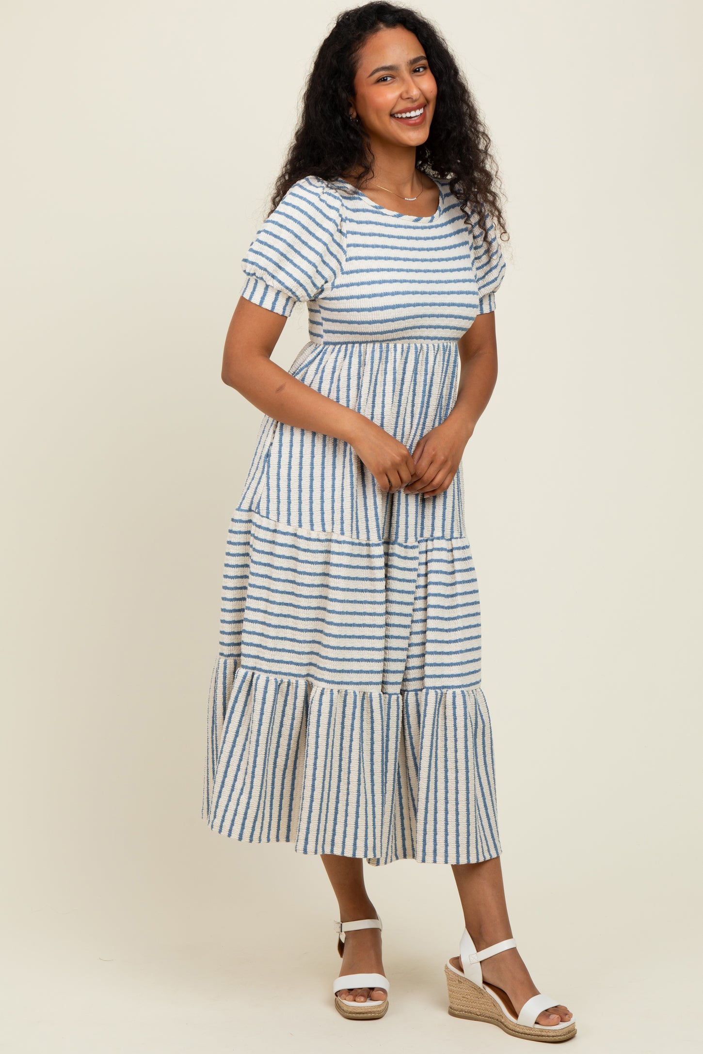 woman wearing a striped midi dress with tiered layers and short sleeves, styled with wedge sandals