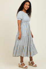 woman wearing a striped blue and white maxi dress with short puff sleeves and tiered skirt, standing in a neutral background