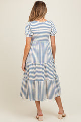 woman wearing a striped blue and white maternity dress with a tiered skirt and puff sleeves, showing a baby bump
