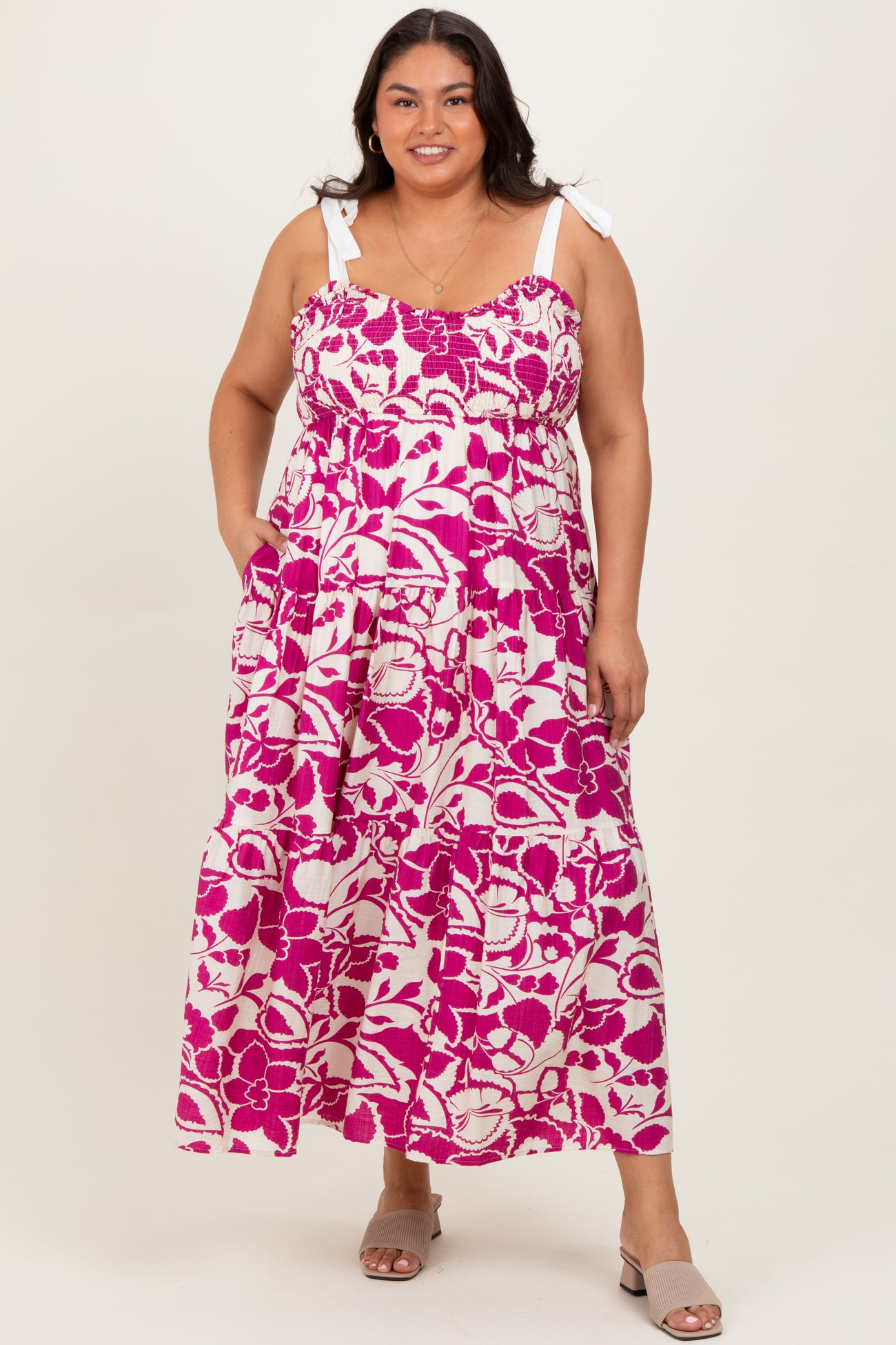 woman wearing a pink and white floral maxi dress with tie straps and pockets, smiling at the camera