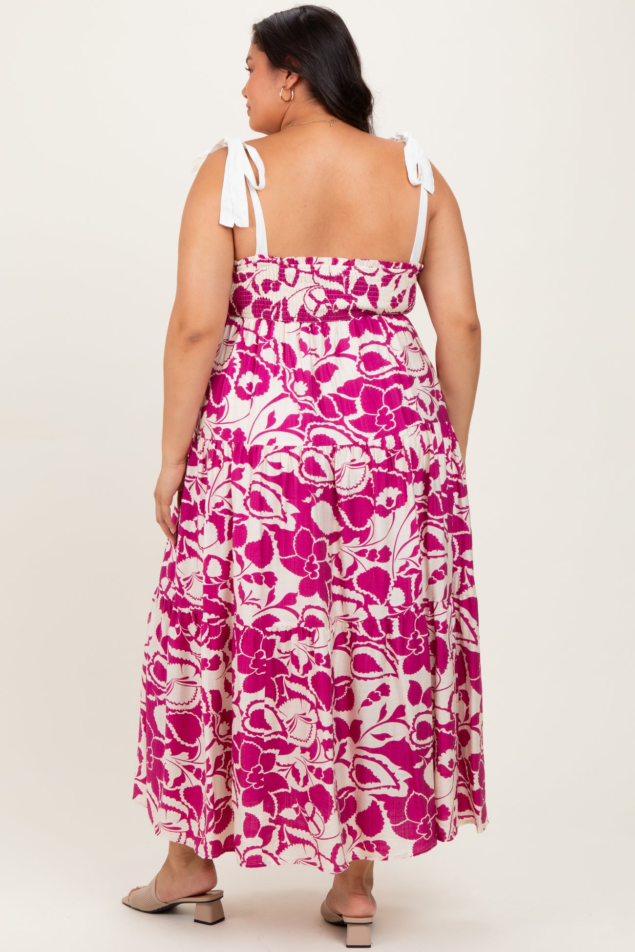 woman wearing a pink and white floral plus size maxi dress with adjustable tie straps, shown from the back