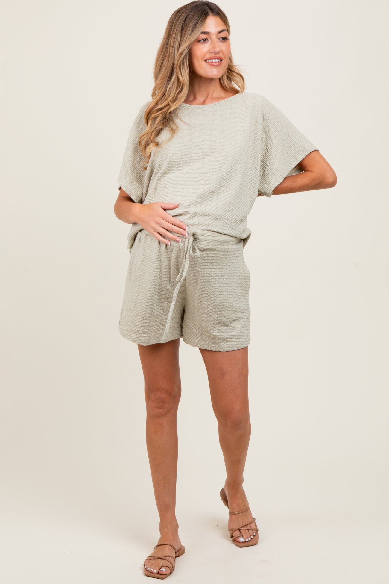 woman wearing a light green maternity shorts set with a loose top and shorts, showing her baby bump
