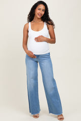 woman wearing a white maternity tank top and light blue flared jeans, gently holding her baby bump