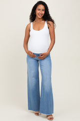 woman wearing a white maternity tank top and light blue flared maternity jeans, showing her baby bump