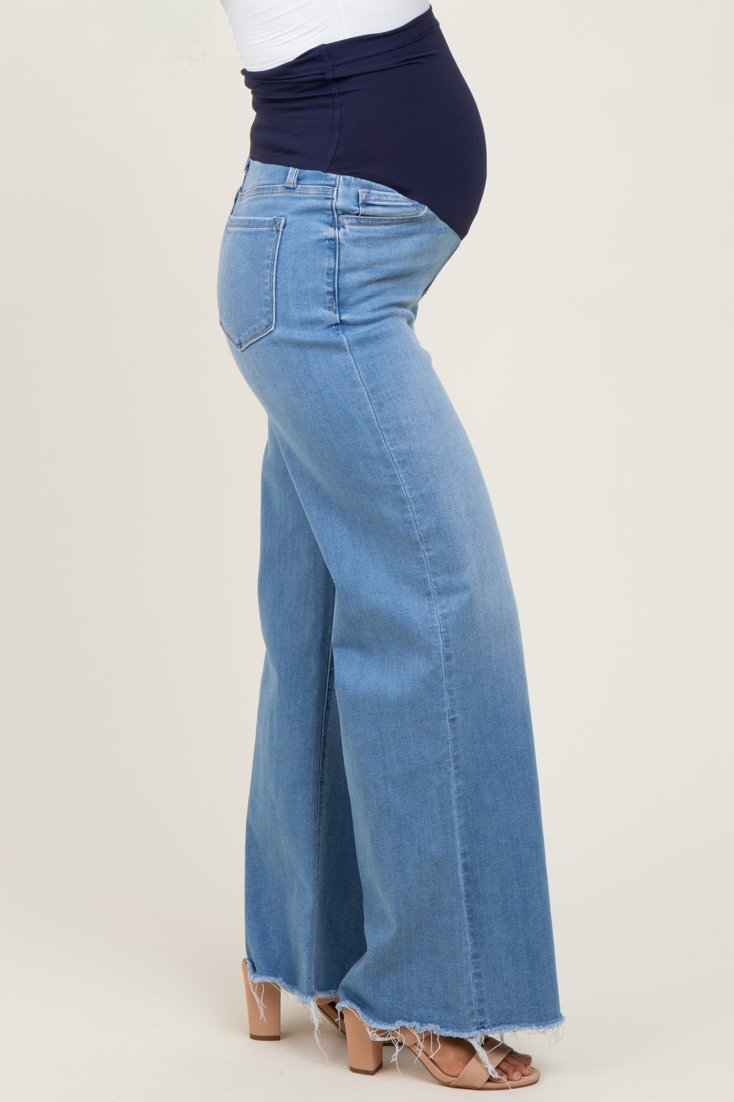 woman wearing a pair of light blue flared maternity jeans with a navy blue belly panel, showing a visible baby bump