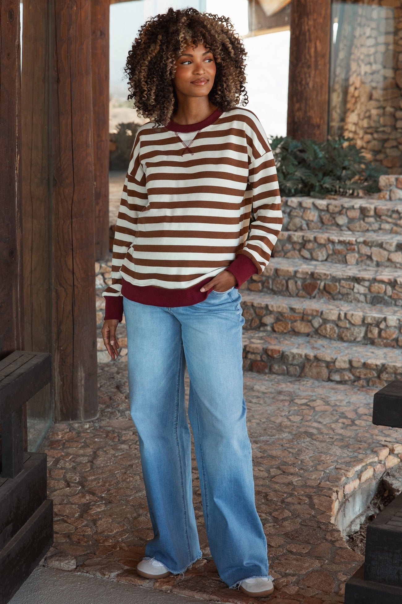 woman wearing a brown and beige striped maternity sweater with a maroon neckline and blue flared maternity jeans