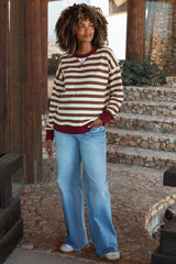 woman wearing a brown and beige striped maternity sweater with a maroon neckline and blue flared maternity jeans