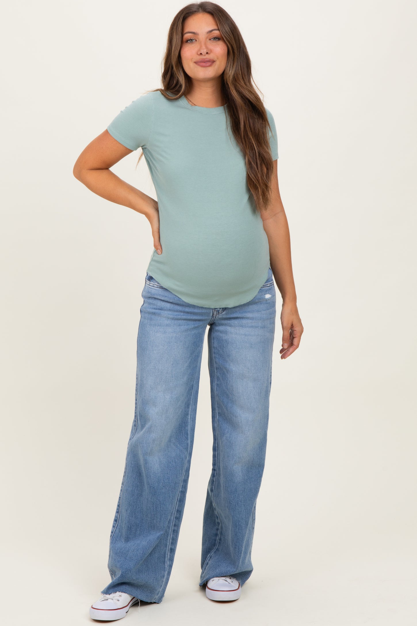 woman wearing a light green short sleeve maternity top and oversized blue jeans, showing her baby bump