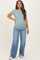 woman wearing a light green short sleeve maternity top and oversized blue jeans, showing her baby bump